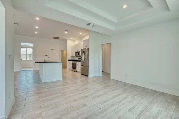 Kitchen featuring white cabinets, an island with sink, dark countertops, stainless steel appliances, and recessed lighting