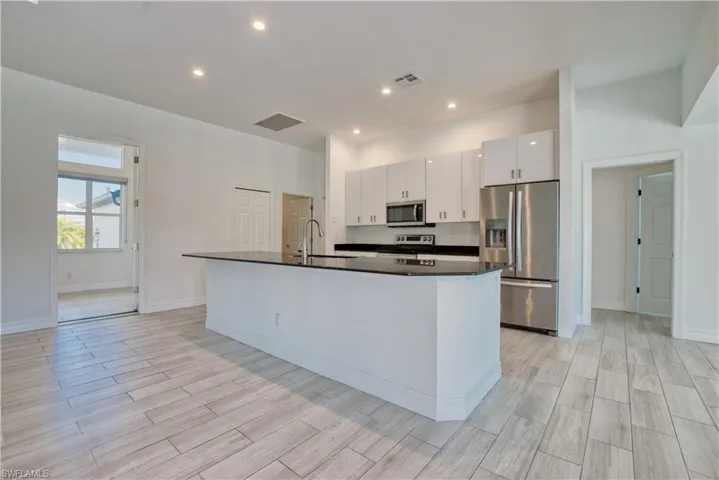 Kitchen with stainless steel appliances, a center island with sink, white cabinets, wood finish floors, and recessed lighting