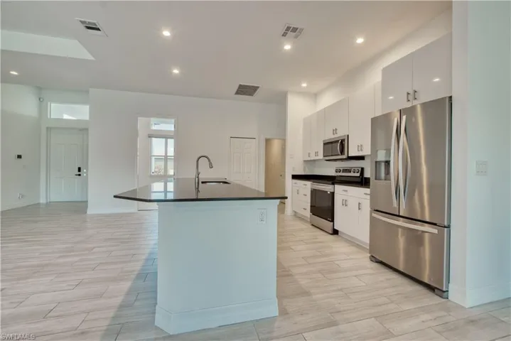 Kitchen featuring stainless steel appliances, wood tiled floors, white cabinets, a kitchen island with sink, and recessed lighting