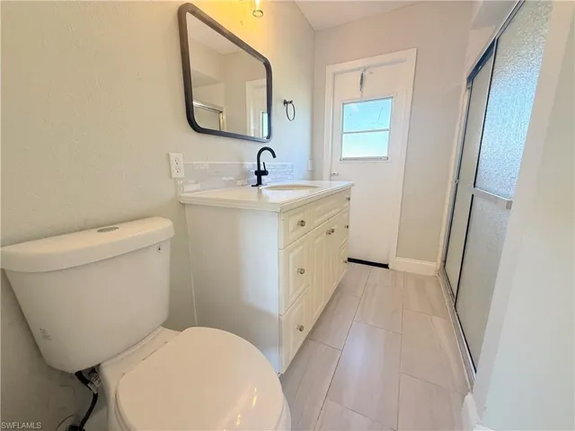 Bathroom with toilet, vanity, a shower with shower door, backsplash, and tile patterned flooring
