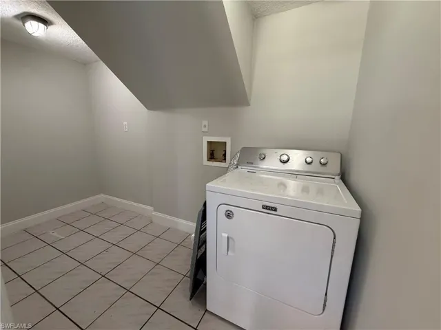 Laundry area with washer / clothes dryer, a textured ceiling, baseboards, and light tile patterned floors