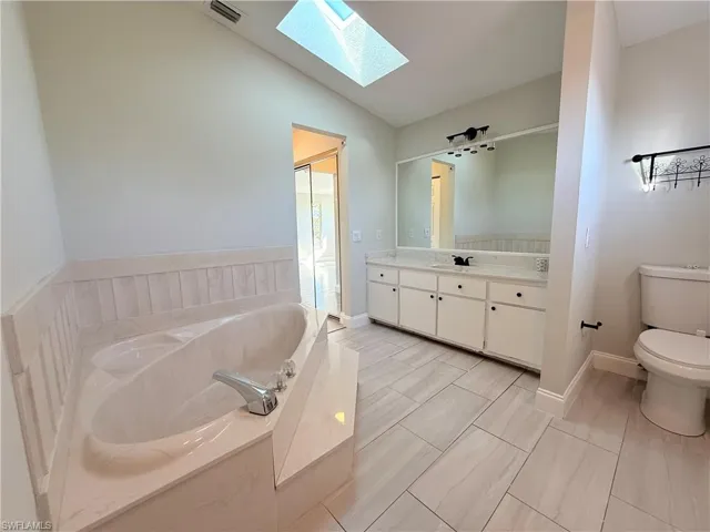 Bathroom featuring a skylight, vaulted ceiling, vanity, a bath, and toilet
