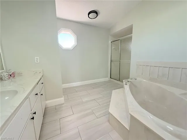 Full bath with a shower stall, a garden tub, vanity, baseboards, and a textured ceiling
