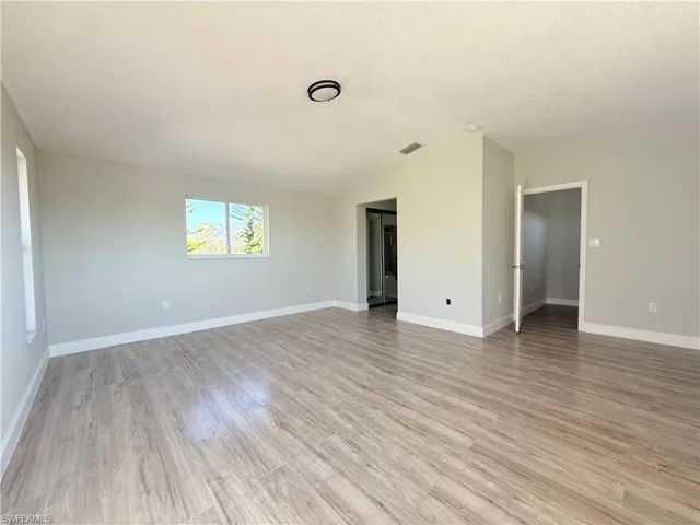 Spare room with vaulted ceiling, light wood finished floors, baseboards, and a textured ceiling