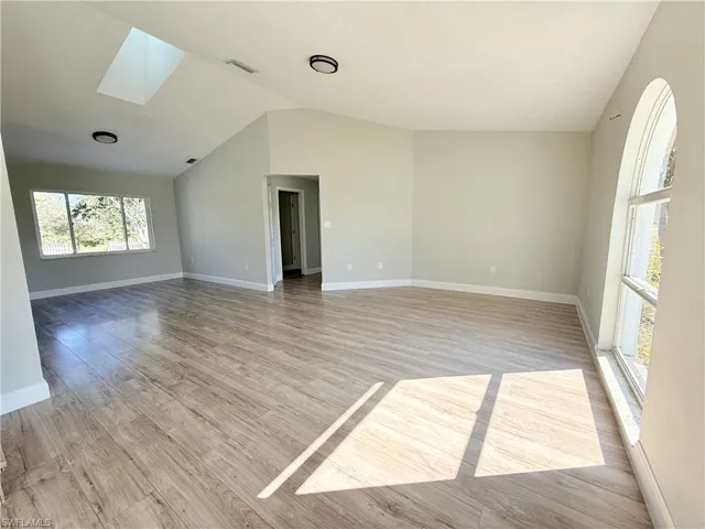 Unfurnished room featuring a skylight, lofted ceiling, light wood-type flooring, and baseboards