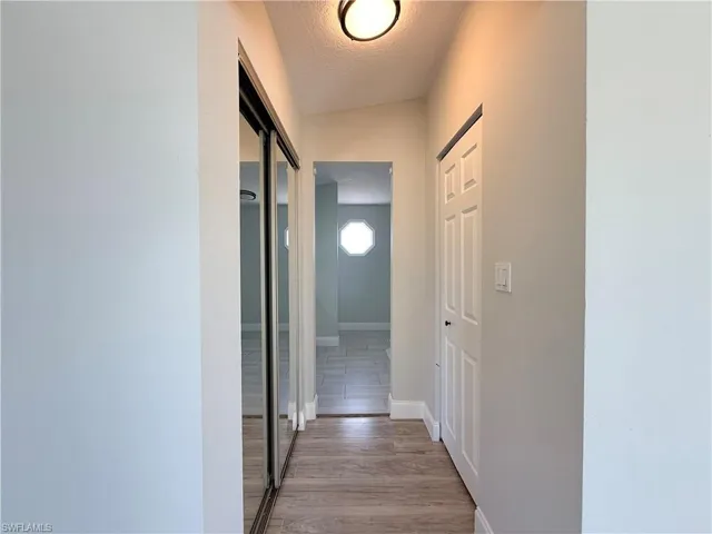 Hall featuring a textured ceiling, light wood-style flooring, and baseboards