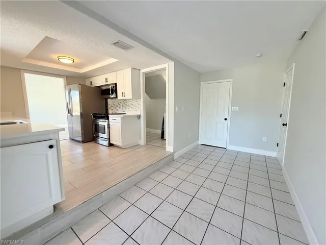 Kitchen featuring stainless steel appliances, light countertops, white cabinets, a textured ceiling, and tasteful backsplash