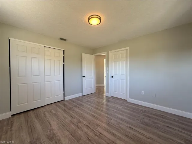 Unfurnished bedroom with baseboards, dark wood-style flooring, a textured ceiling, and a closet