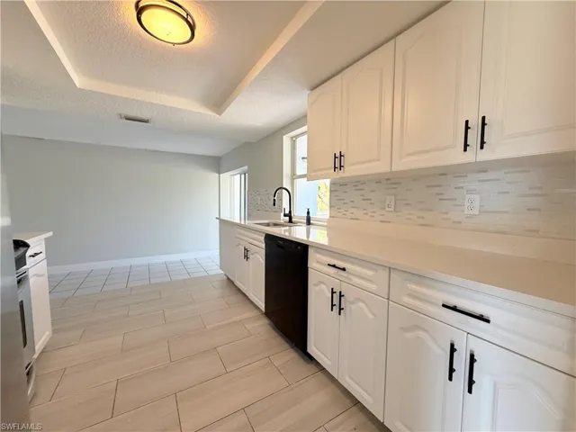 Kitchen featuring dishwasher, a raised ceiling, a sink, decorative backsplash, and a textured ceiling