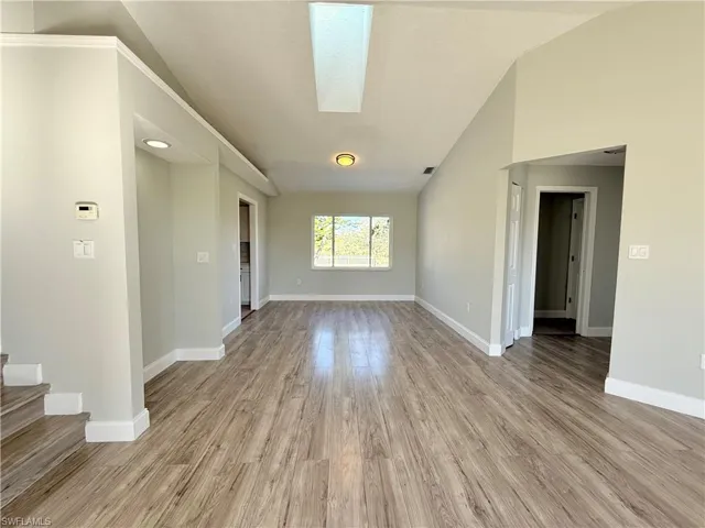 Spare room with light wood finished floors, vaulted ceiling, baseboards, and stairs