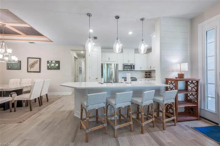 Kitchen with decorative light fixtures, white cabinetry, appliances with stainless steel finishes, a kitchen breakfast bar, and a large island