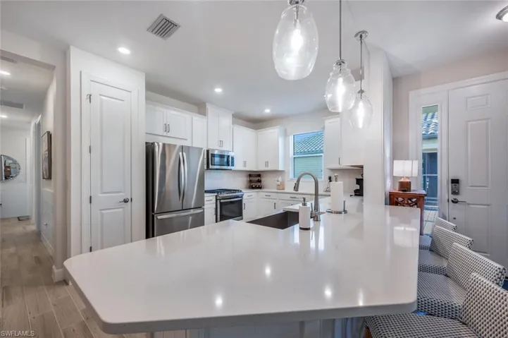Kitchen with appliances with stainless steel finishes, white cabinetry, decorative light fixtures, and sink