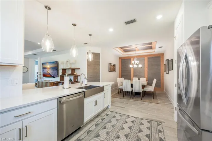 Kitchen featuring decorative light fixtures, appliances with stainless steel finishes, a tray ceiling, and white cabinetry