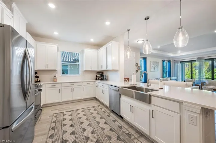 Kitchen with stainless steel appliances, white cabinetry, hanging light fixtures, and sink