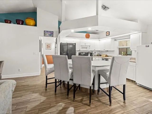 Kitchen featuring white appliances, white cabinets, light wood-type flooring, a breakfast bar area, and a kitchen island