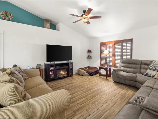 Living room featuring wood finish floors, a glass covered fireplace, ceiling fan, and high vaulted ceiling