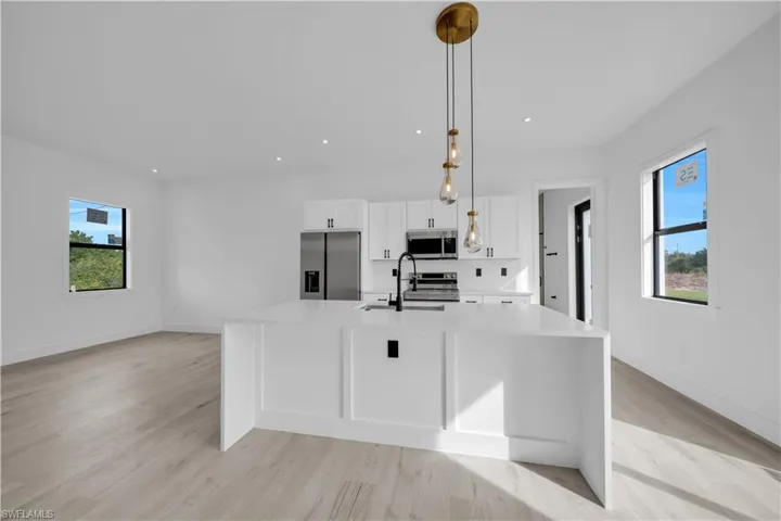 Kitchen featuring healthy amount of natural light, white cabinetry, hanging light fixtures, stainless steel appliances, and recessed lighting