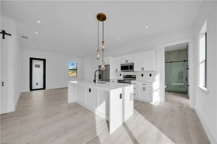 Kitchen with a barn door, an island with sink, pendant lighting, white cabinets, and recessed lighting