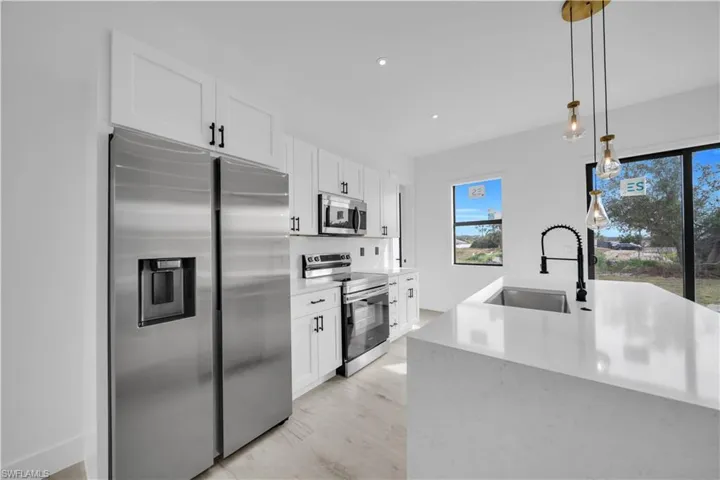 Kitchen featuring stainless steel appliances, white cabinetry, pendant lighting, light stone countertops, and light wood-style flooring