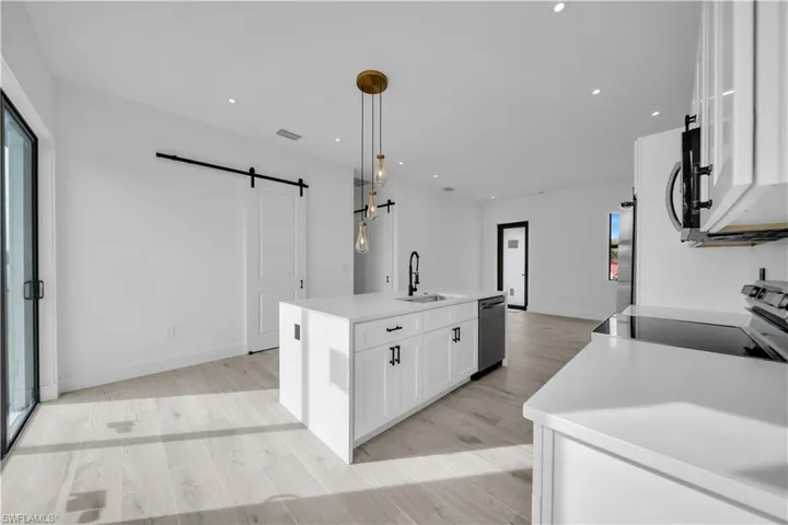 Kitchen with a barn door, white cabinets, decorative light fixtures, recessed lighting, and an island with sink