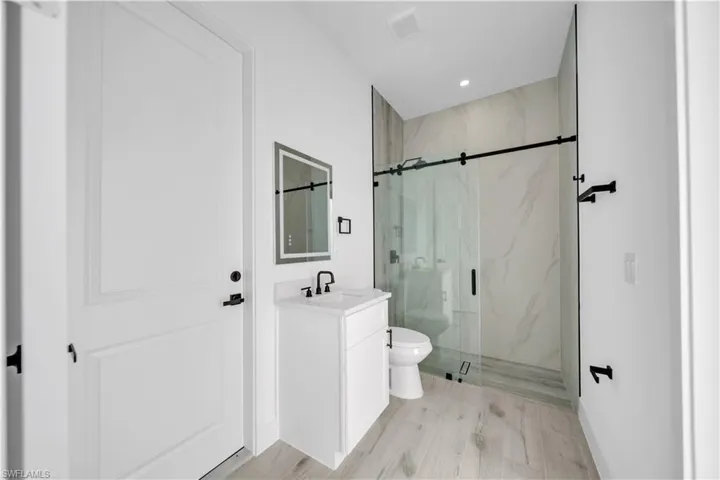 Full bath with a marble finish shower, vanity, light wood-type flooring, and recessed lighting