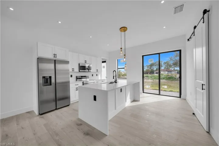 Kitchen with a barn door, appliances with stainless steel finishes, decorative light fixtures, light stone counters, and recessed lighting