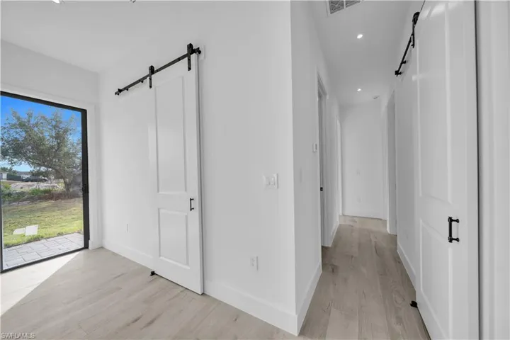 Hall with a barn door, recessed lighting, and light wood-style flooring