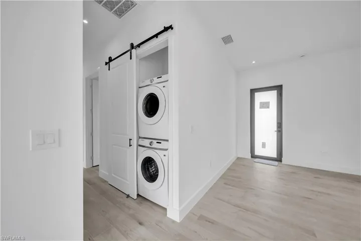 Laundry room with recessed lighting, stacked washer / dryer, a barn door, and light wood-style flooring