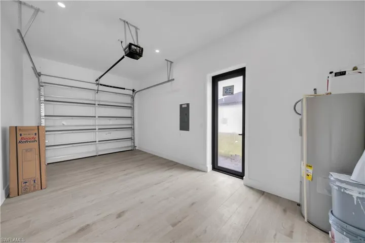 Garage with electric water heater, electric panel, a garage door opener, and recessed lighting