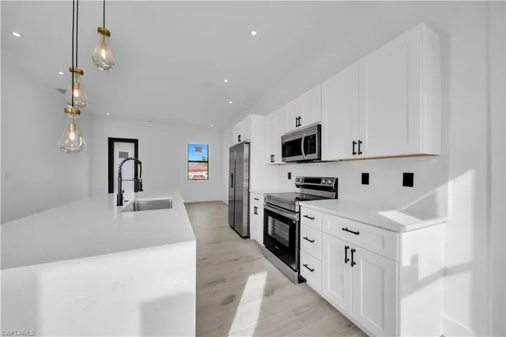Kitchen with stainless steel appliances, decorative light fixtures, white cabinetry, an island with sink, and light stone counters