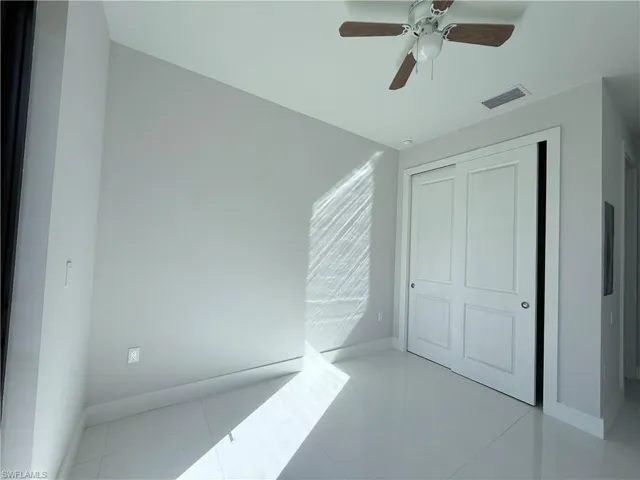 Bright room featuring white tile flooring, light-toned walls, and a ceiling fan with wood-finish blades