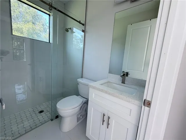 Contemporary bathroom featuring a glass-enclosed shower with a mosaic tile floor, an elongated toilet, a single vanity with a solid surface countertop, an undermount sink, and a rectangular mirror