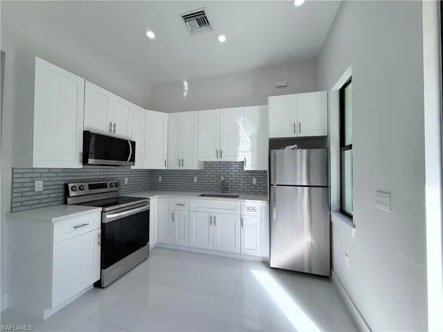Modern kitchen featuring white shaker cabinetry, stainless steel appliances, light-toned countertops, and a gray subway tile backsplash