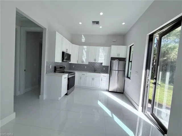 Modern kitchen featuring white cabinetry, stainless steel appliances, a grey subway tile backsplash, and recessed lighting