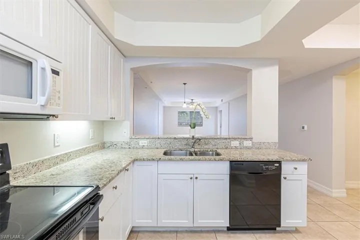 Kitchen with electric range, light stone counters, white cabinets, and black dishwasher