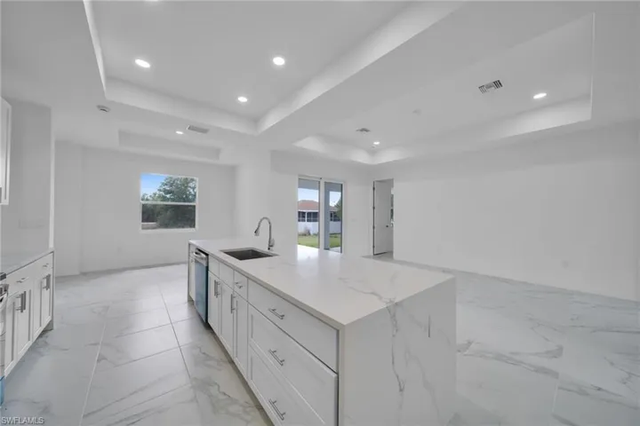 Kitchen island featuring a waterfall-edge countertop, undermount sink, and integrated dishwasher