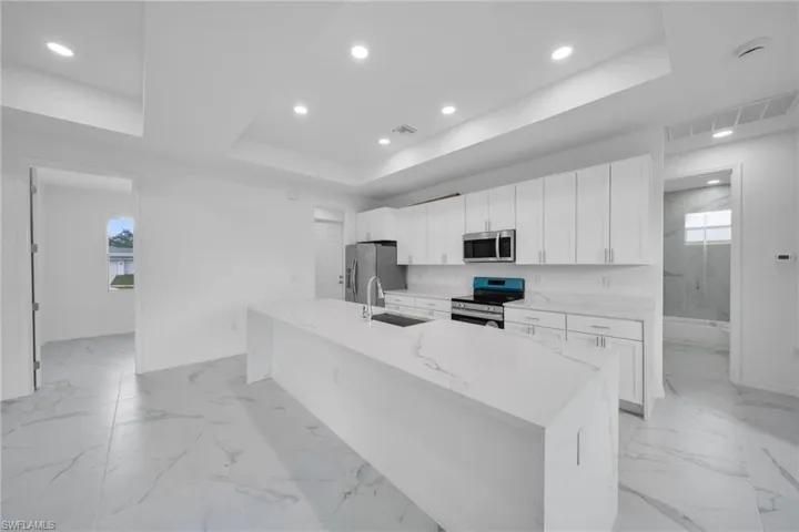 Modern kitchen featuring a waterfall island with stone countertop, white shaker cabinetry, stainless steel appliances, and recessed lighting