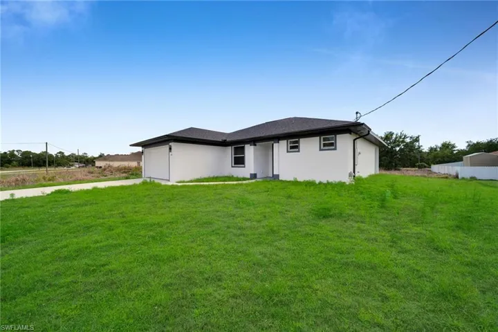 Contemporary single-story exterior with white stucco finish and dark trim accents (grass color has been enhanced)
