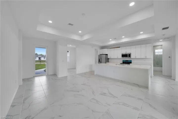 Open concept interior featuring large format tile flooring, a tray ceiling with recessed lighting, an expansive kitchen island with an undermount sink, white flat-panel cabinetry, and stainless steel appliances