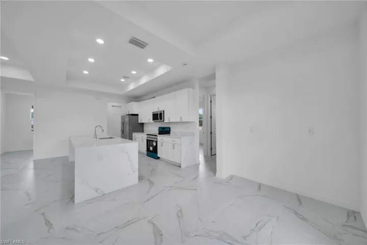 Open-concept kitchen featuring an island with a waterfall-edge countertop, white shaker cabinetry, stainless steel appliances, and large-format porcelain tile flooring