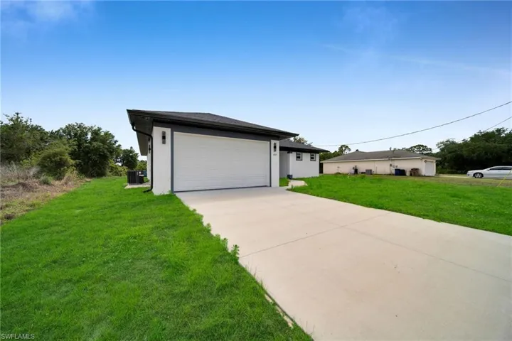 Contemporary exterior featuring a white stucco finish, dark trim, and a prominent two-car garage (grass color has been enhanced)