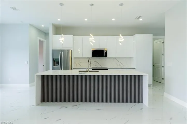 Kitchen with white cabinets, appliances with stainless steel finishes, a kitchen island with sink, marble finish floor, and tasteful backsplash