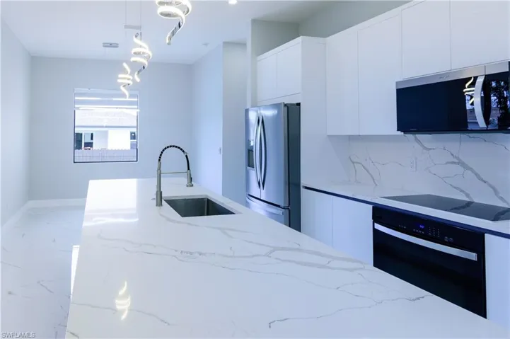 Kitchen featuring appliances with stainless steel finishes, a sink, marble finish floor, white cabinetry, and modern cabinets