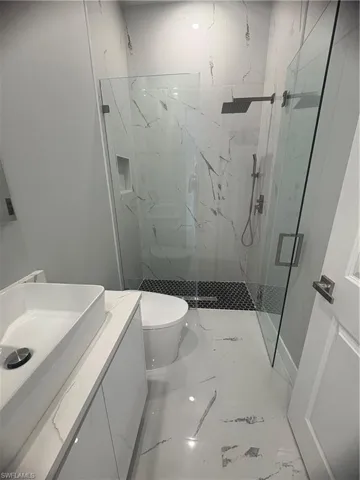 Bathroom featuring vanity, marble finish floor, a marble finish shower, and toilet