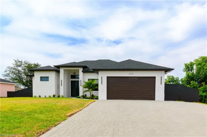 Prairie-style house with fence, an attached garage, a front lawn, stucco siding, and decorative driveway