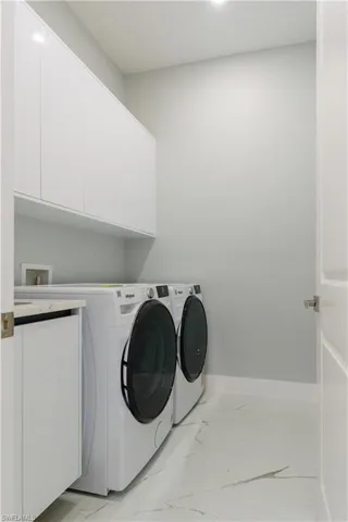 Clothes washing area with baseboards, washing machine and clothes dryer, cabinet space, and marble finish floor