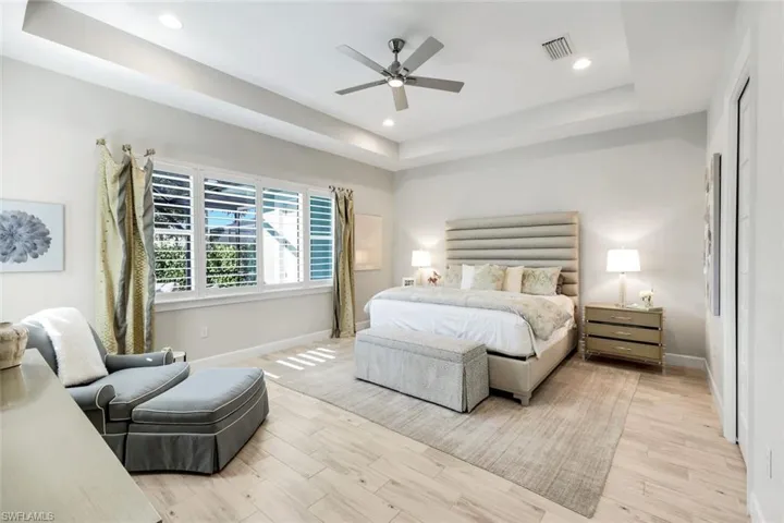 Bedroom featuring a raised ceiling, light wood finished floors, recessed lighting, and ceiling fan