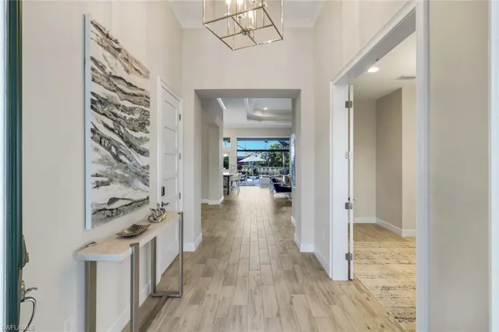 Hall featuring light wood-type flooring, hanging lights, ornamental molding, and a high ceiling