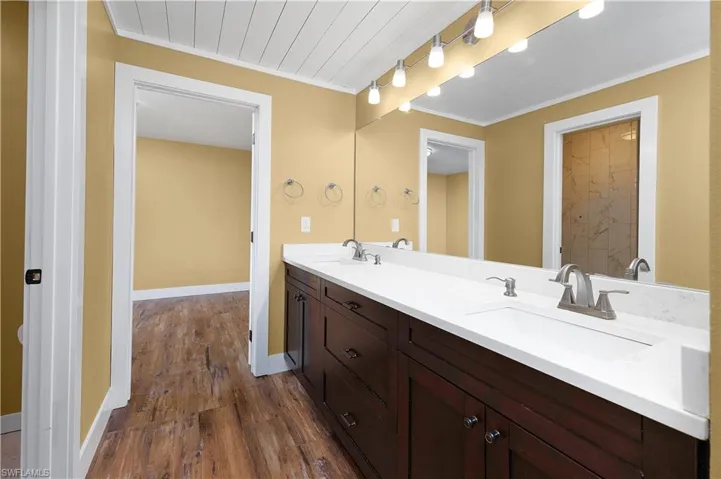 Full bathroom featuring double vanity, dark wood-style flooring, and crown molding