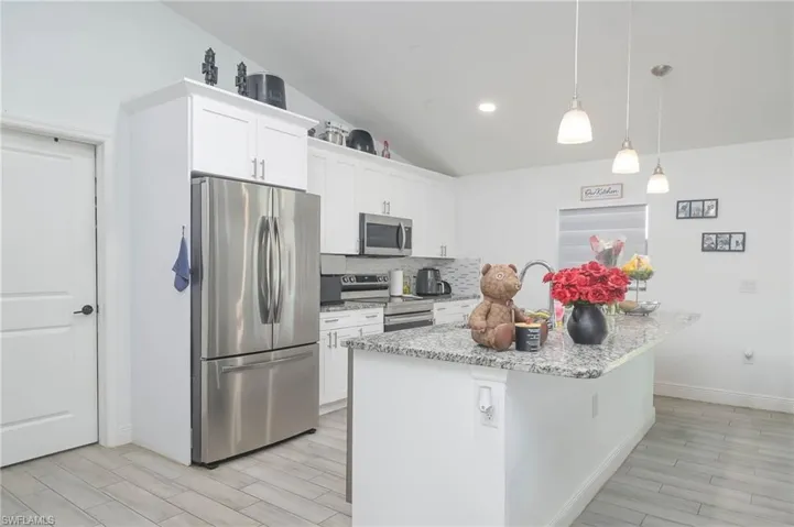 Kitchen with vaulted ceiling, white cabinets, stainless steel appliances, decorative light fixtures, and a center island with sink